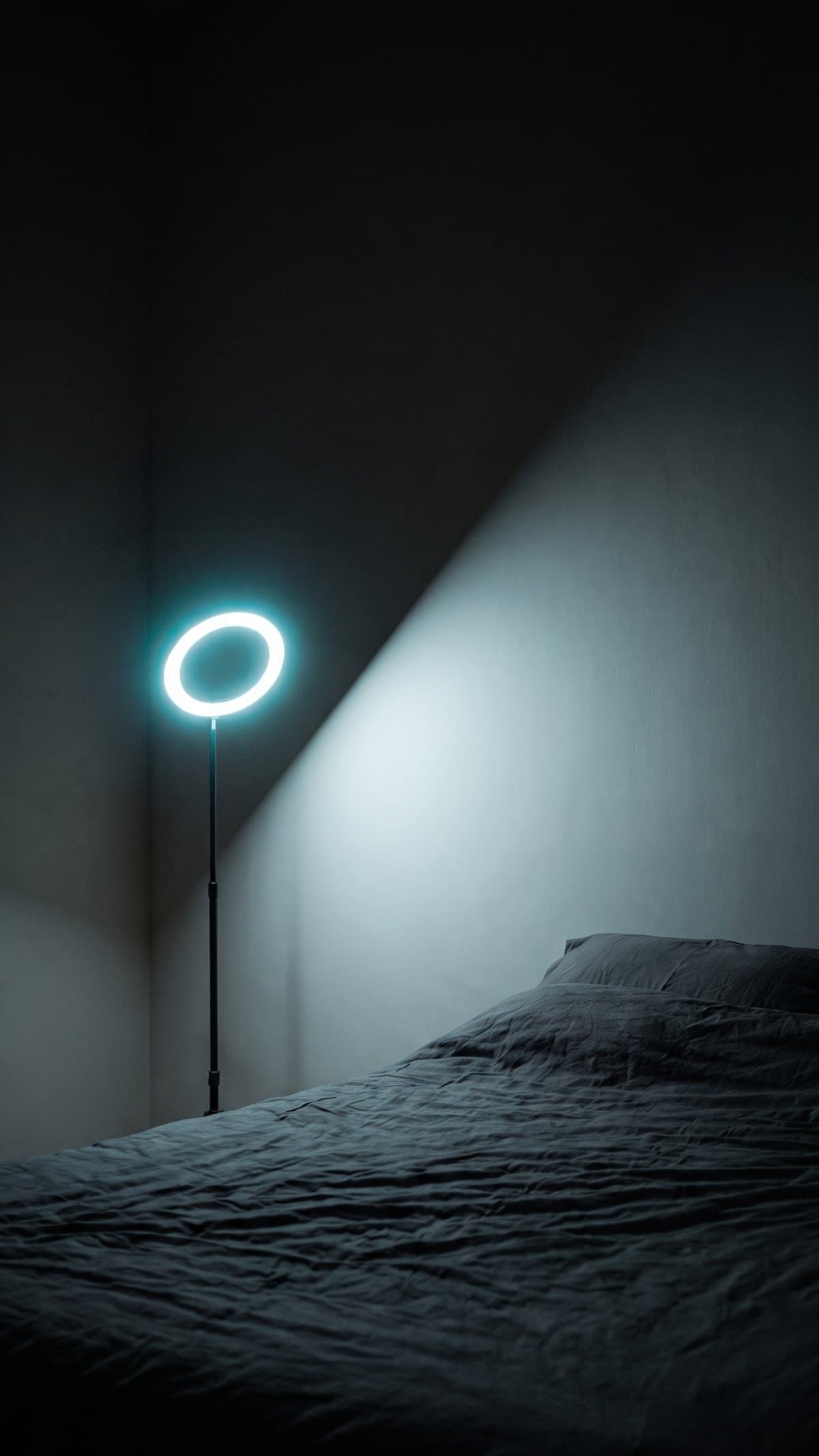 A dark bedroom lit only by a glowing ring lamp in the corner
