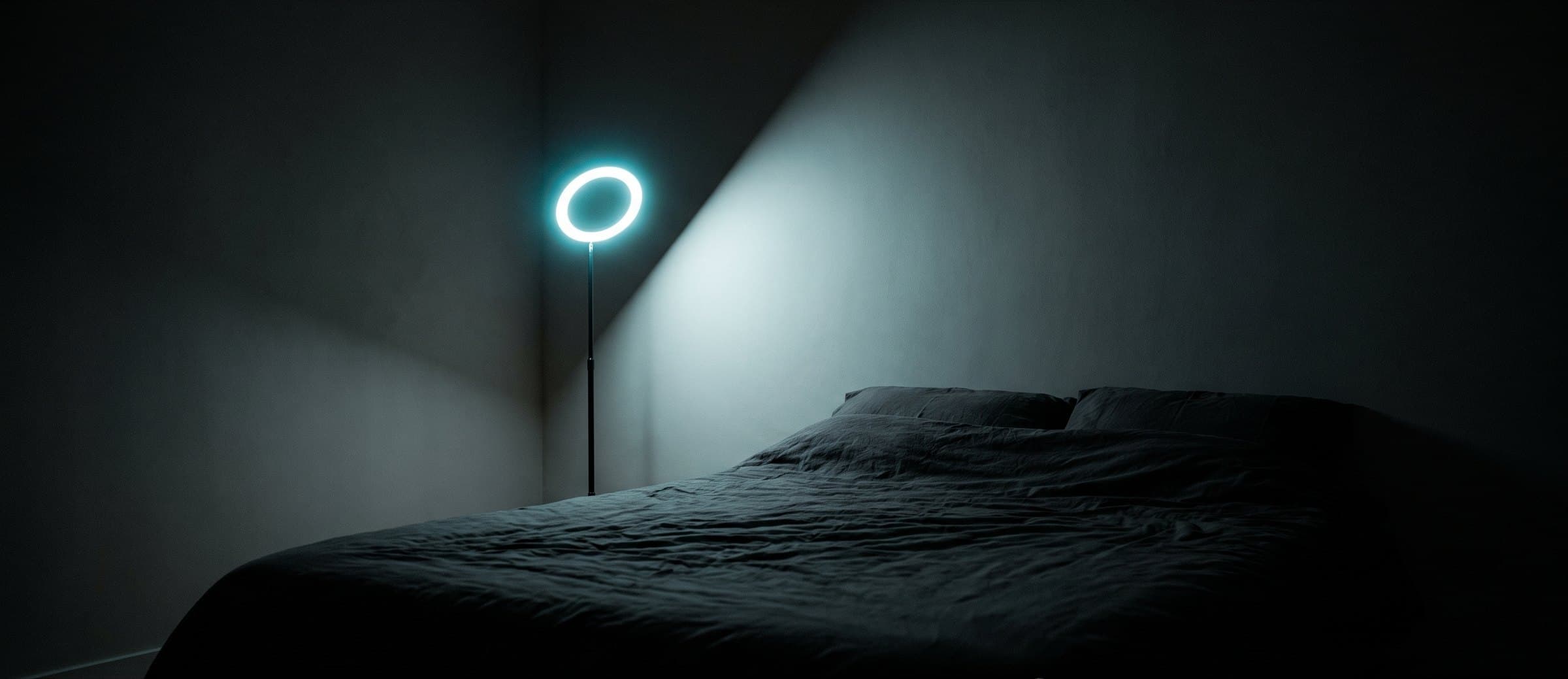 A dark bedroom lit only by a glowing ring lamp in the corner