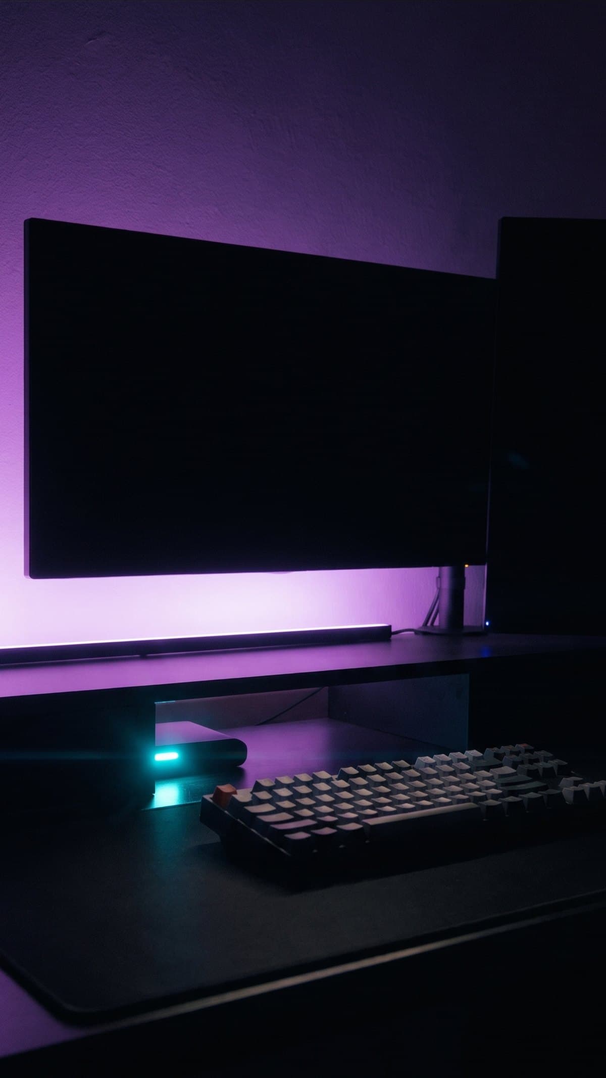 A dark desk setup washed in violet light with the monitors switched off
