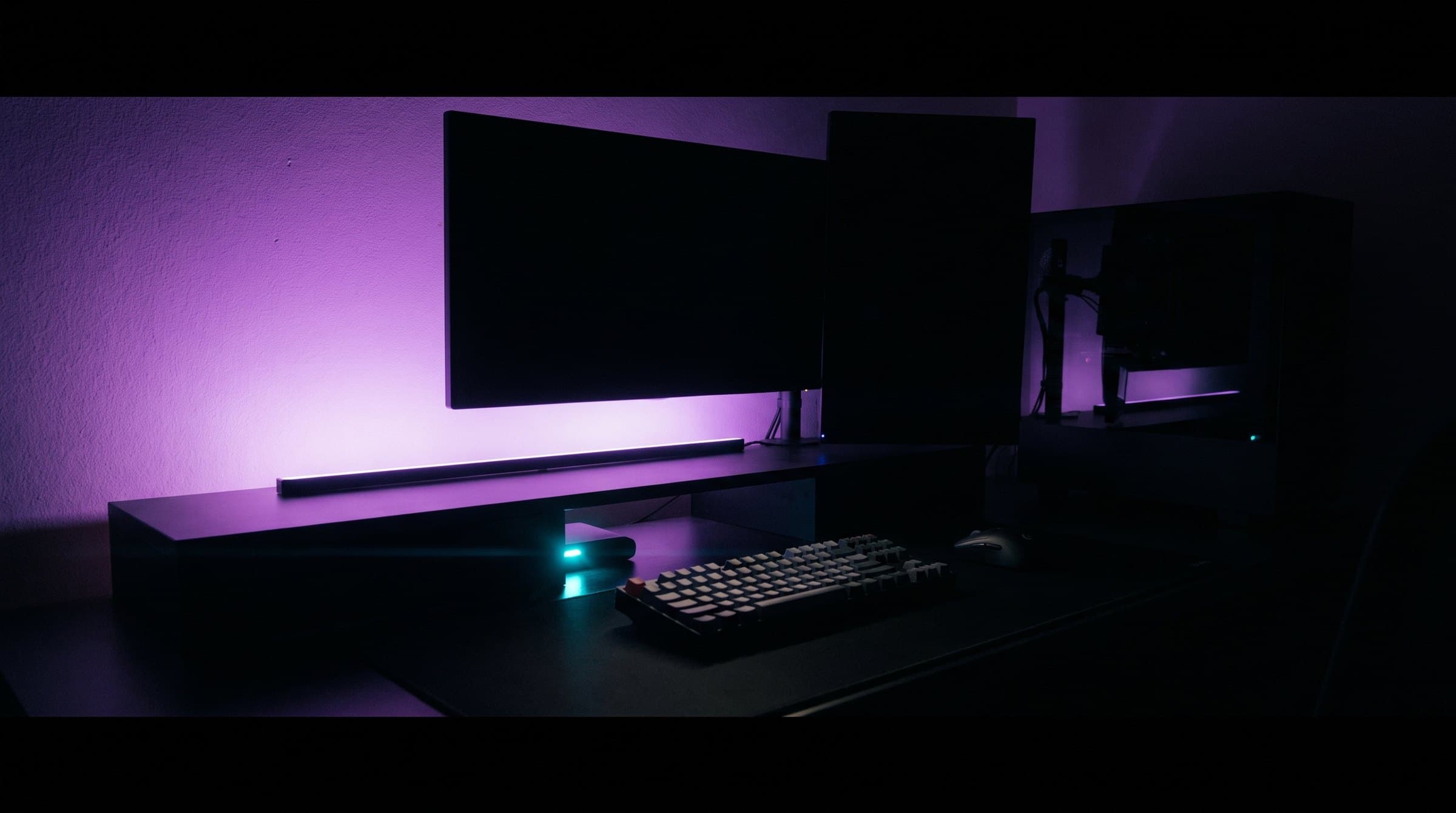 A dark desk setup washed in violet light with the monitors switched off